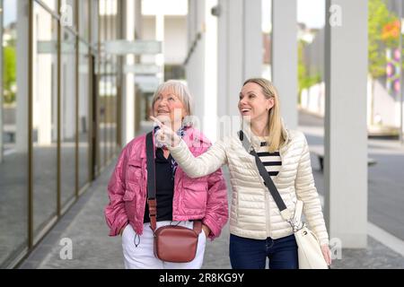 Mère et fille magasinent dans un centre commercial et la fille pointe vers un magasin Banque D'Images