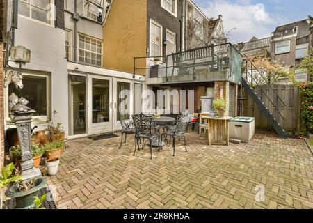 une cour arrière avec meubles de patio et salle à manger extérieure sur un sol en briques parcourus en face de la maison Banque D'Images