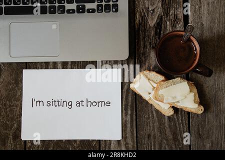 café, pain blanc et beurre sur une table en bois et les mots en anglais sont assis à la maison sur un livre blanc et un ordinateur portable Banque D'Images