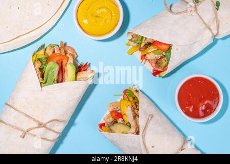 Classique rue nourriture shawarma ou burrito, sandwich sain enveloppé dans la tortilla pain plat avec viande de poulet frite, légumes frais, sauce, sur b vif Banque D'Images