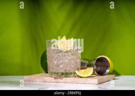 Cocktail d'alcool de punch Ti froid glacé, petit punch, boisson mélangée à base de rhum avec garniture de tranche de citron vert frais, sur fond vert coloré Banque D'Images