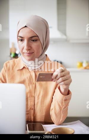 Femme souriante avec hijab tenant la carte de crédit tout en faisant des achats en ligne Banque D'Images