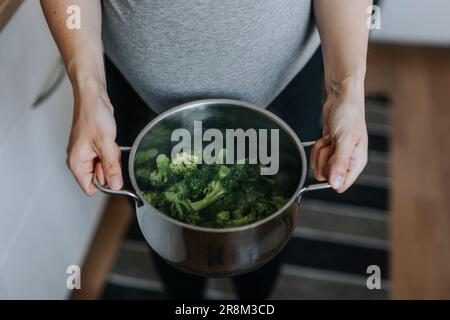 Mains de femme tenant une casserole avec le brocoli bouilli Banque D'Images