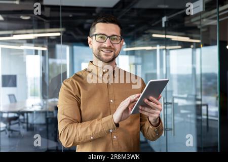 Portrait d'un jeune homme designer debout au bureau et à l'aide d'une tablette. Il regarde la caméra avec un sourire. Banque D'Images