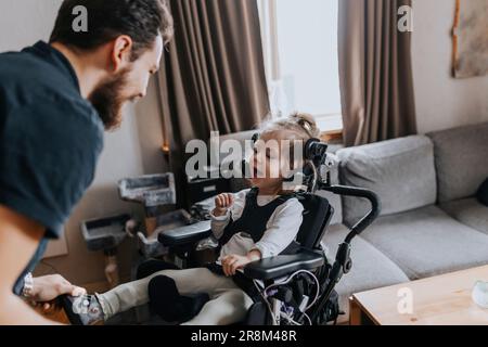 Père prenant soin de sourire enfant handicapé en fauteuil roulant Banque D'Images