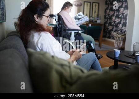 Femme utilisant un téléphone cellulaire sur un canapé, fille adolescente handicapée en fauteuil roulant en arrière-plan Banque D'Images