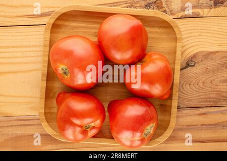 Plusieurs tomates rouges avec plateau en bambou sur table en bois, macro, vue de dessus. Banque D'Images