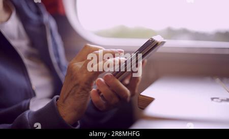 Gros plan des mains d'une femme âgée assise dans un train et utilisant un smartphone Banque D'Images