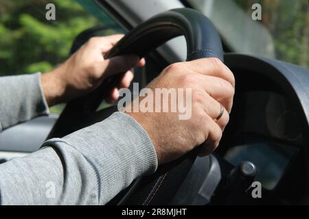 Mains mâles tenant le volant de direction de près. Homme confiant conduisant une voiture pendant un voyage de jurney. Vue latérale depuis l'intérieur du véhicule côté passager. Jour d'été. Banque D'Images
