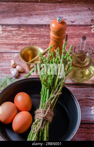 Bouquet d'asperges sauvages dans une poêle avec œufs, ail, huile d'olive et poivre, ingrédients pour faire une omelette Banque D'Images