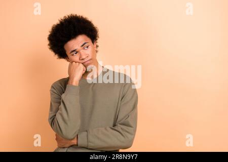 Photo d'esprit jeune homme insatisfait de la main toucher joue look vide espace isolé sur fond beige couleur Banque D'Images