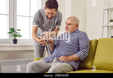 Jeune infirmière brune aidant un patient âgé à utiliser un smartphone. Banque D'Images