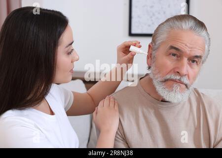 Une jeune femme goutte des médicaments dans l'oreille de l'homme à la maison Banque D'Images