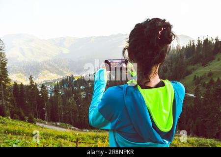 Hipster fille est en tournage vidéo photo de beau lever de soleil sur téléphone cellulaire, tandis que est debout contre fond ciel lumineux avec espace de copie. Banque D'Images