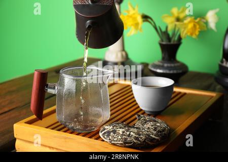 Verser le thé pu-erh fraîchement préparé dans le pichet pendant la cérémonie traditionnelle à une table en bois Banque D'Images