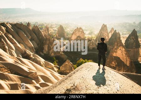 Un stand de femme attentif vous permet de regarder la vallée spectaculaire sur un lever de soleil brumeux avec des cheminées de fées en arrière-plan. Exploration solo en Turquie Banque D'Images