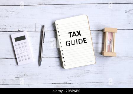 Vue de dessus du stylo, de la calculatrice, du sablier et du carnet écrit avec "GUIDE FISCAL" sur fond blanc en bois. Banque D'Images