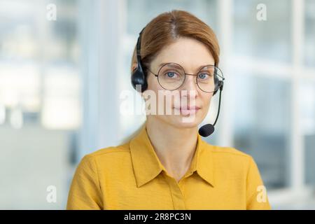 Portrait d'une jeune enseignante portant des lunettes et un casque. Assis au bureau et regardant la caméra. Effectue des formations à distance en ligne. Gros plan. Banque D'Images