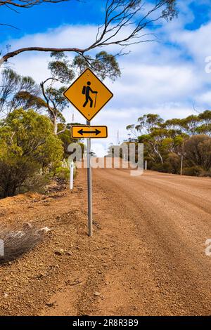 Panneau d'avertissement le long d'une route de gravier dans l'Outback australien : le sentier de randonnée traverse la route. Banque D'Images