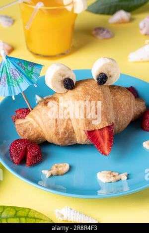 Nourriture amusante pour les enfants - croissant en forme de crabe avec fraise et banane sur plaque bleue sur fond jaune Banque D'Images