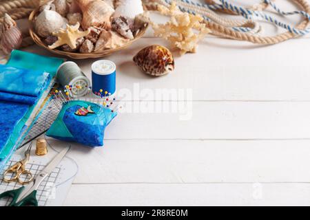 Accessoires de couture et panier avec coquillages sur une surface en bois blanc, espace pour le texte Banque D'Images
