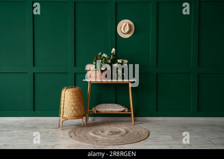 Panier en osier avec fleurs de jasmin sur la table de console près du mur vert Banque D'Images