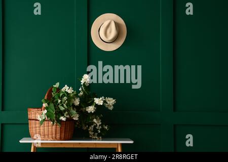 Panier en osier avec fleurs de jasmin sur la table de console près du mur vert Banque D'Images