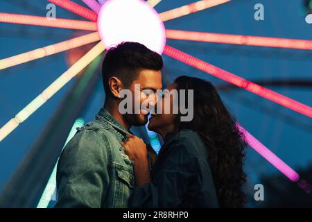 Vue latérale du jeune couple heureux contre la grande roue la nuit Banque D'Images