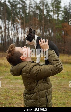 Le garçon tient son chien bien-aimé sur ses bras tendus et des baisers. Marcher avec un animal de compagnie. Amitié d'un enfant avec un chien. Banque D'Images