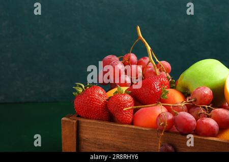 Boîte en bois avec différents fruits frais sur table verte Banque D'Images