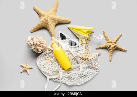 Sac à cordes avec lunettes de soleil, mini-parapluie, corail et bouteille de crème solaire sur fond gris Banque D'Images