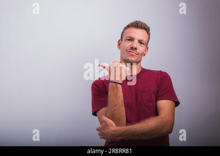 Un jeune homme pointe son pouce vers l'espace à gauche, photo de publicité studio avec espace de copie Banque D'Images