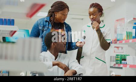 Afro-américain homme en fauteuil roulant achetant des médicaments de pharmacie, venant en pharmacie avec une travailleuse sociale féminine. Client parlant au spécialiste du traitement de la maladie, magasin de détail. Prise de vue à main levée. Banque D'Images