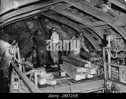 Les mineurs de roche travaillent sur la plate-forme supérieure du jumbo de tunnel dans le tunnel Eucumbene Tumut. Le jumbo a trois plates-formes et un quatrième groupe d'hommes travaillent depuis le sol du tunnel. 1949:le projet Snowy Mountains a été lancé. ***** comme l'un des plus grands travaux de génie civil en cours ***** dans le monde. La fin des travaux est prévue pour 1975, les sources d'eau de Snowy.***** coût du projet. 29 avril 1955. (Photo de S.M.H.E.A. Photo officielle). Banque D'Images