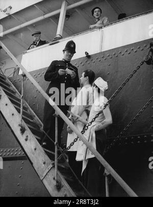 Inspection des passes à Beaverbrae -- Un policier en service au navire canadien Beaverbrae inspectant les passes des marins canadiens (non grévistes) à bord du navire à Royal Victoria Dock, à Londres jusqu'à aujourd'hui (mardi), premier jour de la réglementation sur l'état d'urgence aux quais de Londres. La Beaverbrae et un autre navire canadien, l'Argomont, ont été impliqués dans une grève des marins canadiens. Parce que les dockers de Londres refusent de travailler sur eux et les employeurs de quai disent que les navires canadiens doivent être travaillés avant tout otehrs plus de 10 000 hommes sont maintenant inactifs dans le port de Londres et 112 navires détenus… Banque D'Images