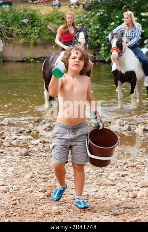 Voyageur jeune garçon transportant le seau pour laver les chevaux dans la rivière eden annuel appleby voyageurs gitan traditionnel Horse Fair juin 2023 cumbria. Banque D'Images