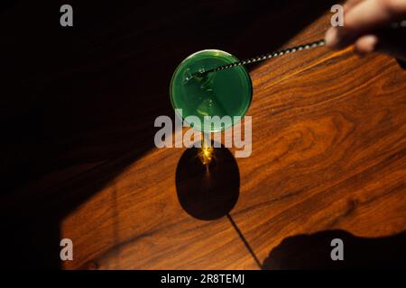 brasser à la main l'absinthe verte dans un verre coupé avec une cuillère à barres argentées sur une table en bois au soleil Banque D'Images