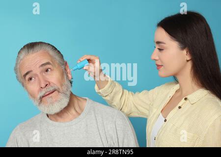 Une jeune femme goutte des médicaments dans l'oreille de l'homme sur fond bleu clair Banque D'Images