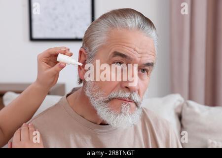 Une jeune femme goutte des médicaments dans l'oreille de l'homme à la maison Banque D'Images