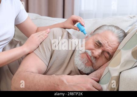 Une jeune femme goutte des médicaments dans l'oreille de l'homme à la maison Banque D'Images