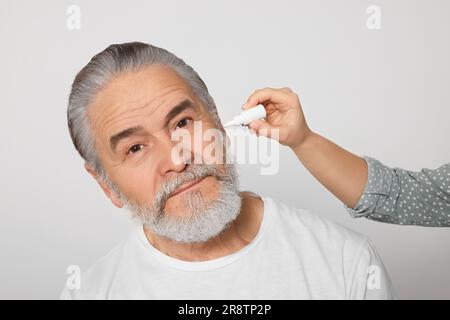 Une jeune femme goutte des médicaments dans l'oreille de l'homme sur fond blanc Banque D'Images