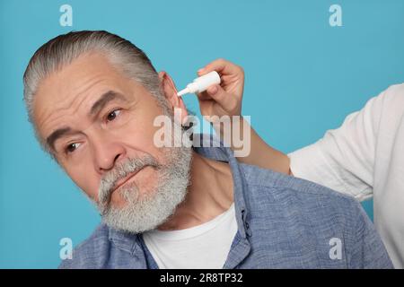 Une jeune femme goutte des médicaments dans l'oreille de l'homme sur fond bleu clair Banque D'Images