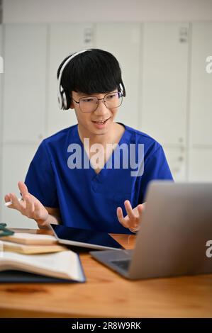 Un étudiant ou un médecin asiatique spécialisé en médecine masculine dans les exfoliations portant des écouteurs est d'avoir un examen médical en ligne avec un patient ou de se joindre à un nous médical Banque D'Images