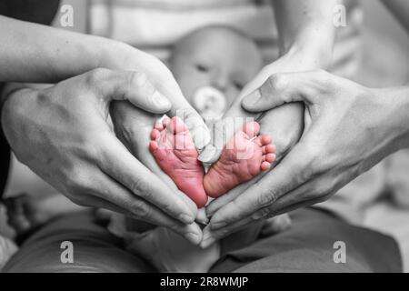 Doux nouveau-né famille formant bébé pieds coeur les pieds de bébé dans la mère et le père parent mains sélectives couleur. Banque D'Images