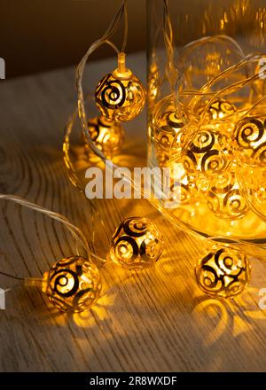 Guirlande de boules en métal doré dans un pot en verre sur fond de table en bois clair. Guirlande lumineuse de Noël jaune or avec ampoules LED. La guirlande du nouvel an. Pour Banque D'Images