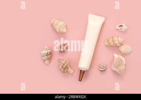 Visage et yeux crème squeeze tube cosmétique avec buse longue et bouchon à vis en bronze et différentes coques de mer beaucoup sur fond rose. Vue de dessus avant. Plat Banque D'Images