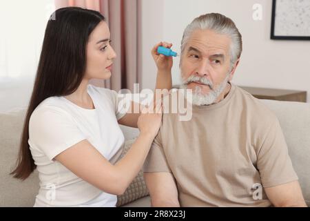 Une jeune femme goutte des médicaments dans l'oreille de l'homme à la maison Banque D'Images