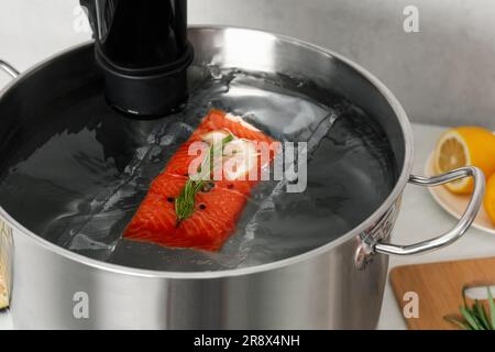 Sous vide cuisinière et saumon emballé sous vide dans une casserole sur table, gros plan. Circulateur à immersion thermique Banque D'Images