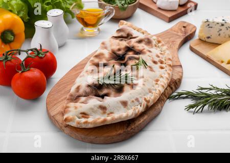 Savoureuse pizza calzone au romarin et différents produits sur table carrelée de blanc Banque D'Images