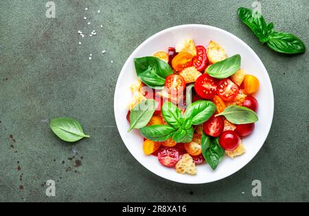 Salade de légumes d'été panzanella avec pain rassis, tomates colorées, huile d'olive, sel et basilic vert, fond de table vert, vue du dessus Banque D'Images